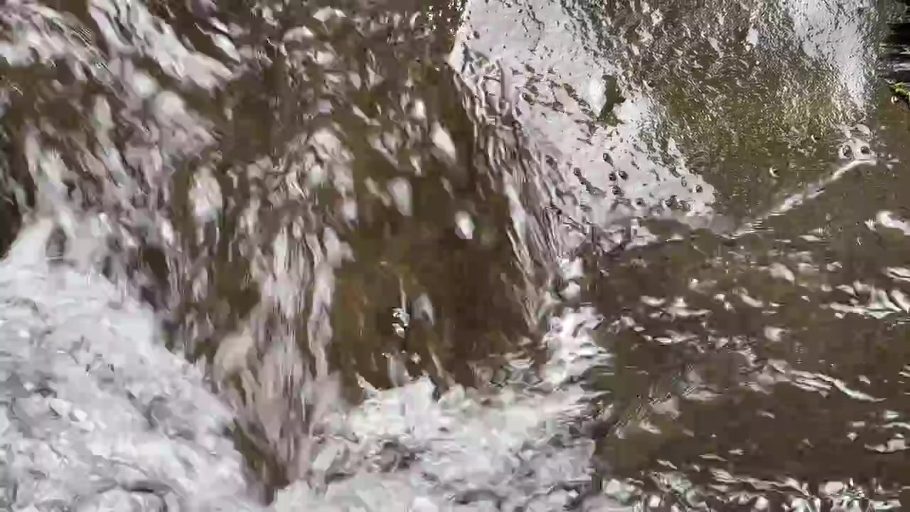 Primo piano dell'acqua che scorre su rocce scure in un ruscello