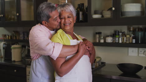 una feliz pareja biracial con delantales abrazándose en la cocina