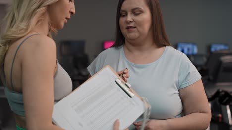 adult female trainer measuring fat layer of overweight woman with waistline at fitness club.