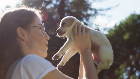 joven caucásica con gafas sosteniendo un cachorro labrador en el parque en un día de verano