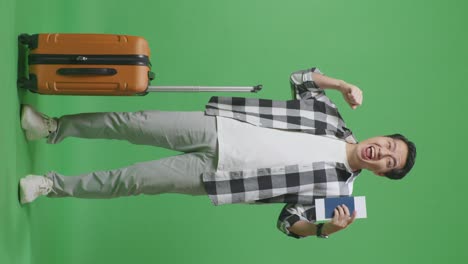 full body of asian male traveler with luggage and passport screaming goal celebrating while standing in the green screen background studio