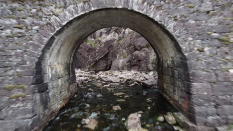 flying through arch of old traditional stone bridge at road fv569 besides hesjedalsfossen waterfall - woman swimming in pond on other side - western norway