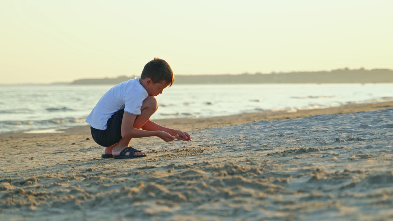Side view of young boy doing something on the sea coast in the evening. Summer vacation scene of child playing in the sand beach.