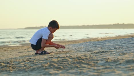side view of young boy doing something on the sea coast in the evening. summer vacation scene of child playing in the sand beach.