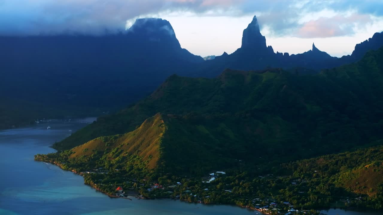 Golden hour sunset Cooks Opunohu Bay Moorea island French Polynesia aerial drone clouds covering Mount Mauaroa Tohivea Rotui clouds lagoon coral reef waves Pacific Ocean backwards