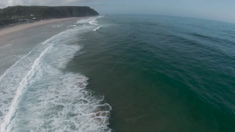 Vista-Aérea-De-Las-Olas-Rompiendo-Durante-Un-Concurso-Mundial-Con-Montañas-Al-Fondo