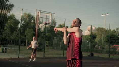 In-The-Foreground,-A-Concentrated-Male-Basketball-Player-Doing-Deltoid-And-Tricep-Stretch-Excercises