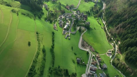 eine schräge luftansicht der kurvenreichen straßen, die durch die steilen, mit gras bedeckten hügel des kleinen dorfes la val in südtirol, italien, führen