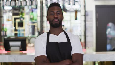 Retrato-De-Un-Barista-Afroamericano-Sonriendo-A-La-Cámara-Usando-Delantal-En-La-Cafetería