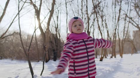 Cheerful-child-girl-kid-walking,-smiling,-dancing-on-snowy-road-in-winter-sunny-park-forest,-sunset