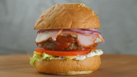 One-hamburger-on-a-board-fries-are-scattered-around.-Close-up-of-delicious-fresh-home-made-burger-with-lettuce-cheese-onion-and-tomato-on-a-rustic-wooden-plank-on-a-dark-background