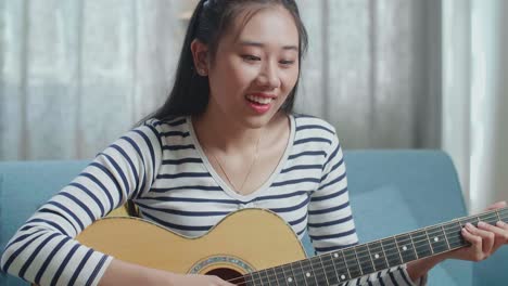 close up of asian woman learning playing guitar by a laptop at home