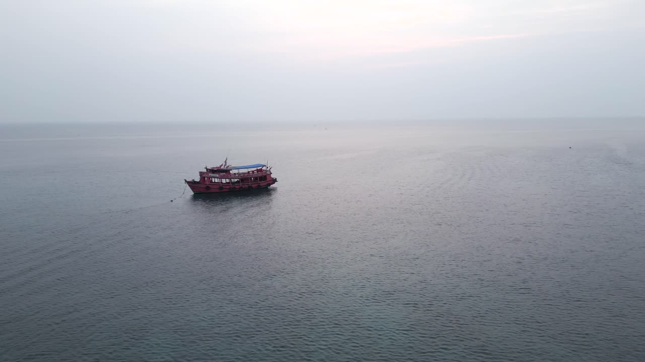 A red boat anchored in a calm bay with an island in the background
