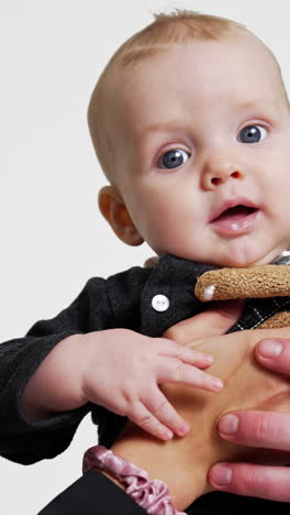 male and female hands hold beautiful smiling caucasian infant. mother and father kiss their lovely son on the head. white backdrop. vertical video