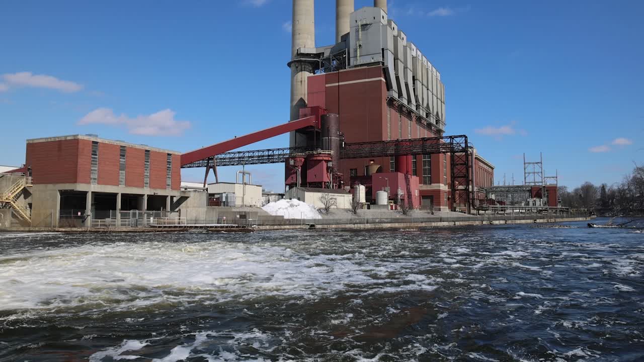 Coal burning power plant with three smoke stacks tilting down to river in slow motion.