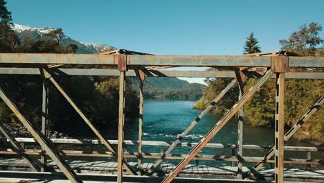 Drohne-Steigt-Aus-Dem-Wasser-Auf-Die-Spitze-Einer-Alten-Metallbrücke,-Um-Die-Herbstlandschaft-Mit-Dem-See-Im-Hintergrund-Zu-Sehen