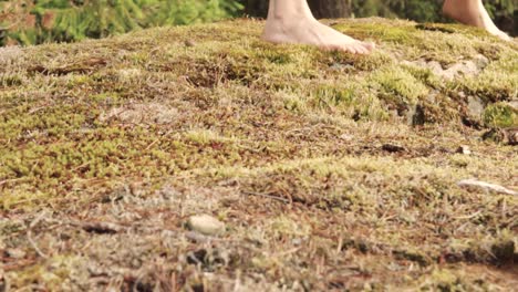 los pies descalzos de un joven bailan o hacen yoga en el suelo del bosque cubierto de musgo.
