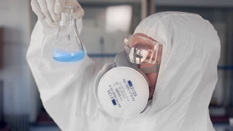 scientist in a protective suit and a respirator examines a blue substance in a test tube