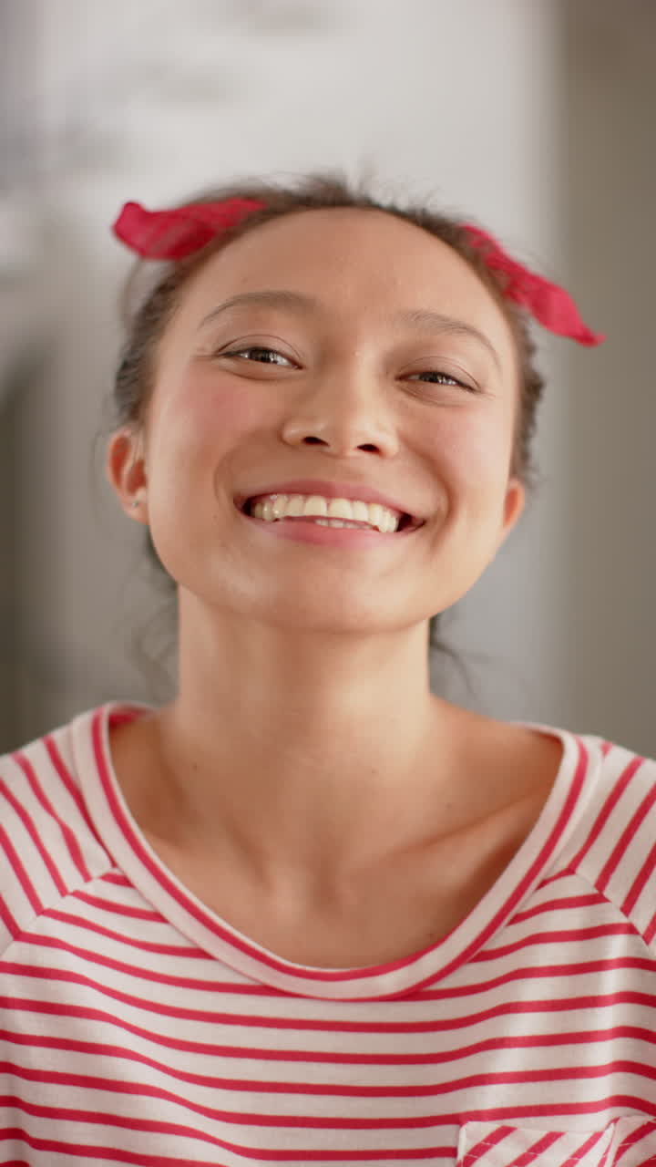 Vertical video of portrait of happy asian woman with headband, smiling at home, slow motion