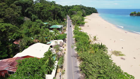 A cinematic overhead shot of a road of travelers and tourists driving down the beach Playa Cocles revealing the popular tourist destination Puerto Viejo on the Caribbean coast of Costa Rica.