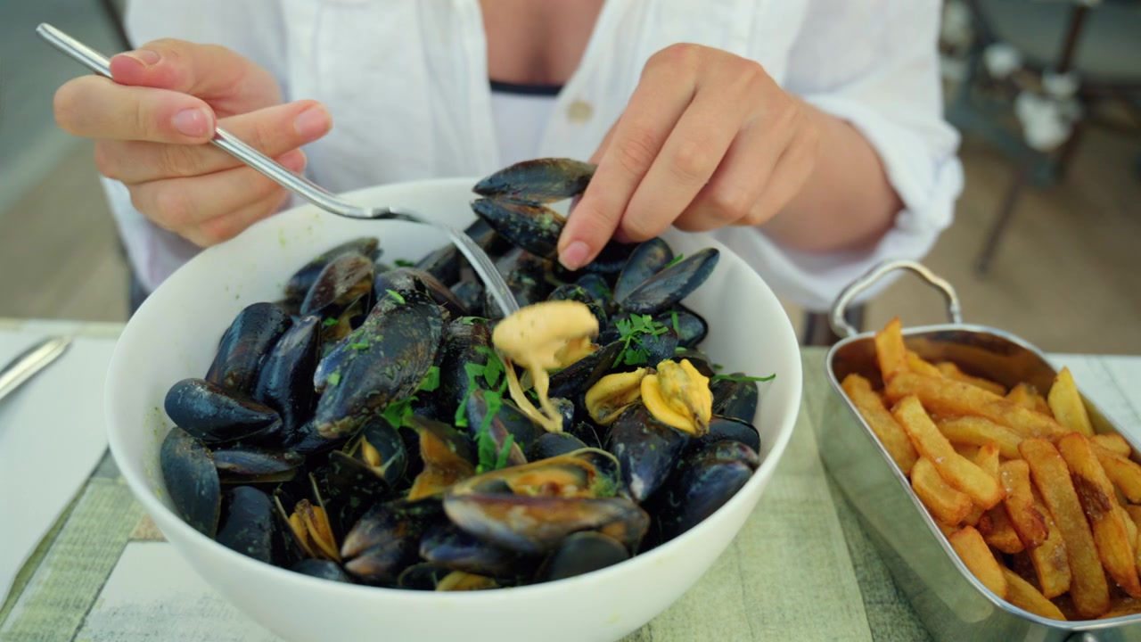 Woman eating a traditional serving of steamed mussels with fresh parsley and golden fried potatoes at a restaurant