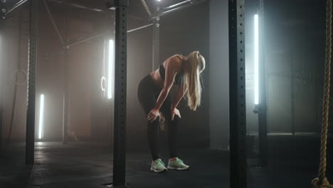 Mujer-Joven-Descansando-Después-De-Su-Entrenamiento-Y-Mirando-Hacia-Abajo.-Atleta-Femenina-Descansando-Después-Del-Entrenamiento-Físico-En-El-Gimnasio-Oscuro