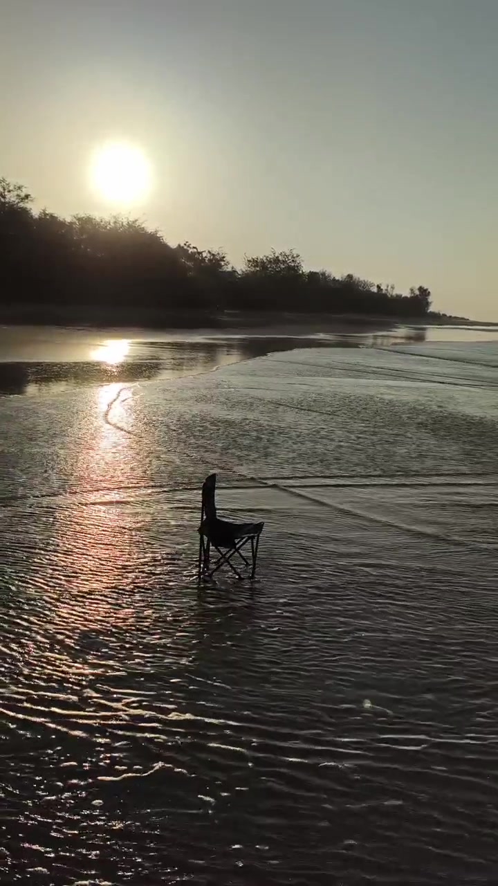 Empty Folding Chair Standing in Shallow Ocean Waves at Sunset