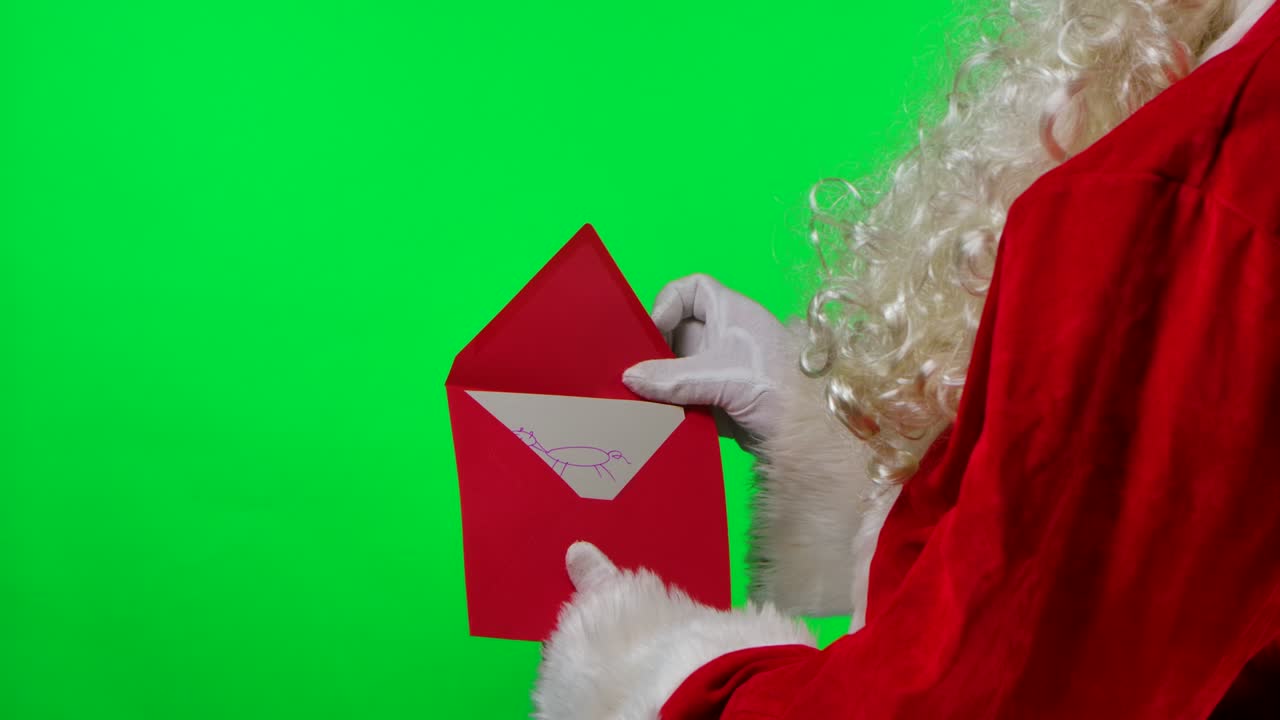 Papai Noel com barba, luvas brancas e terno vermelho segurando um envelope com uma carta de uma criança. Isolado em tela verde em um estúdio. Chroma key. Close-up. Câmera lenta.