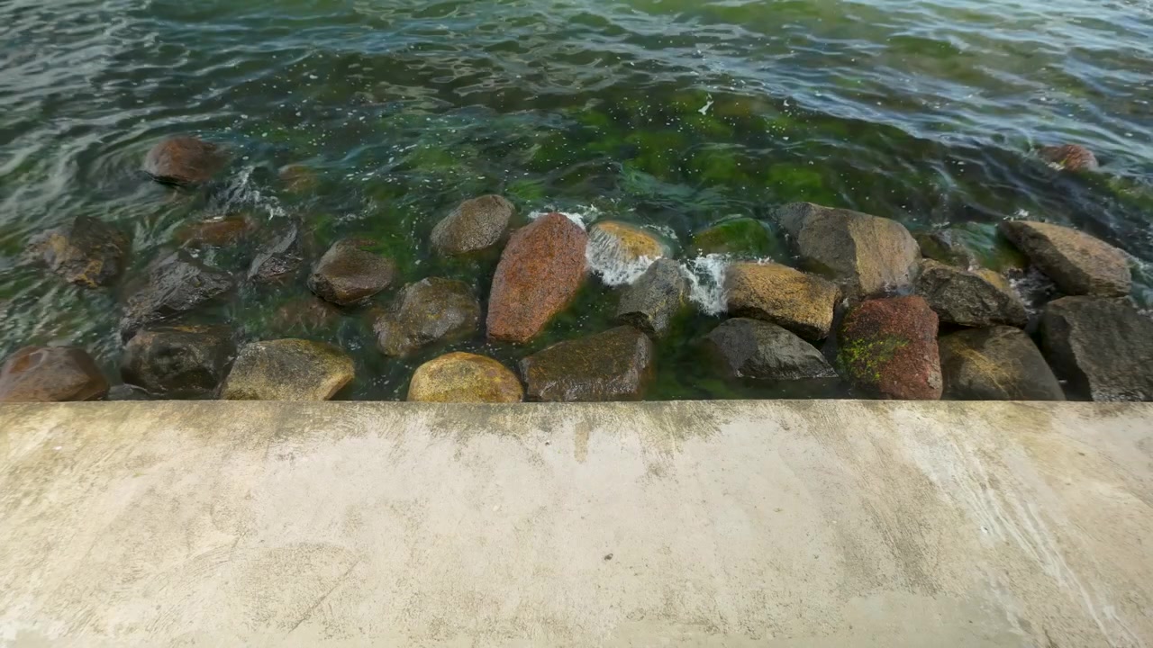 Et rolig syn av milde havbølger som slår mot en steinete molo under en lys himmel, egnet for reise- og naturinnhold