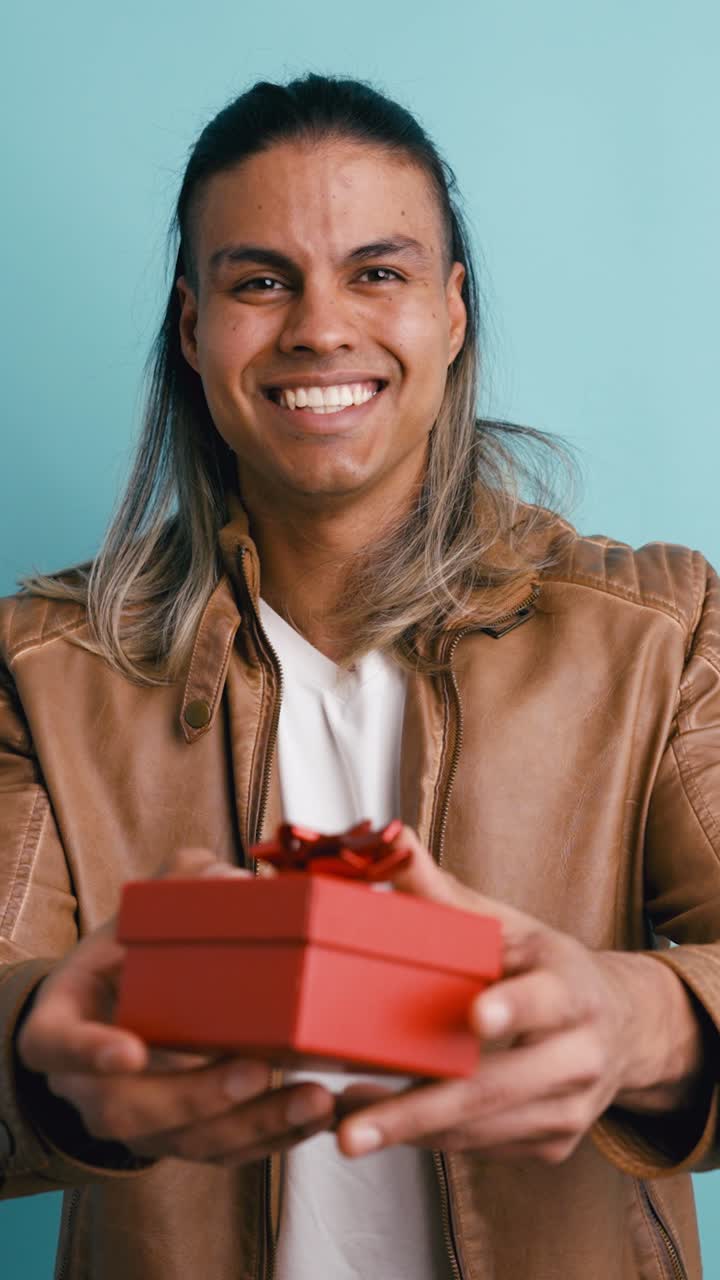 Giovane uomo che sorride e offre una scatola regalo rossa