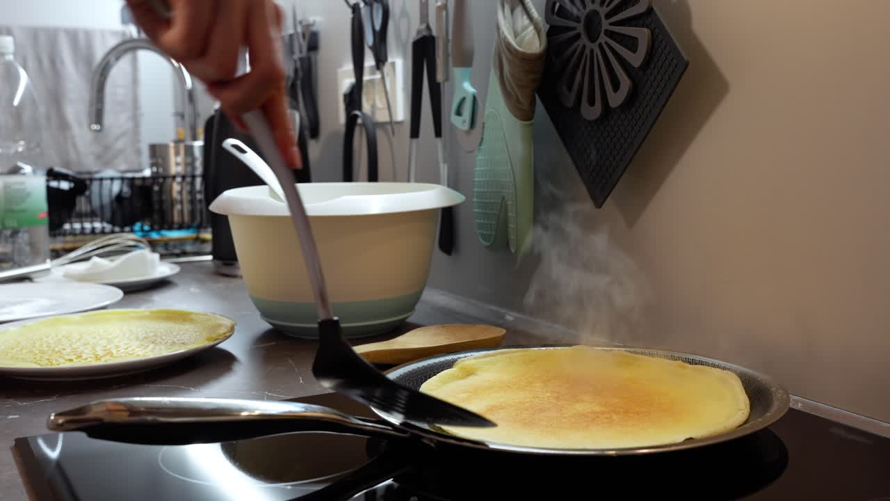 Steaming hot European pancake removed from flat frying pan on stove top, closeup