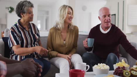 Zwei-Unterschiedliche-Seniorenpaare-Sitzen-Zu-Hause-Auf-Einer-Couch-Und-Trinken-Gemeinsam-Tee