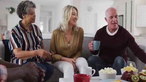 two diverse senior couples sitting on a couch drinking tea together at home