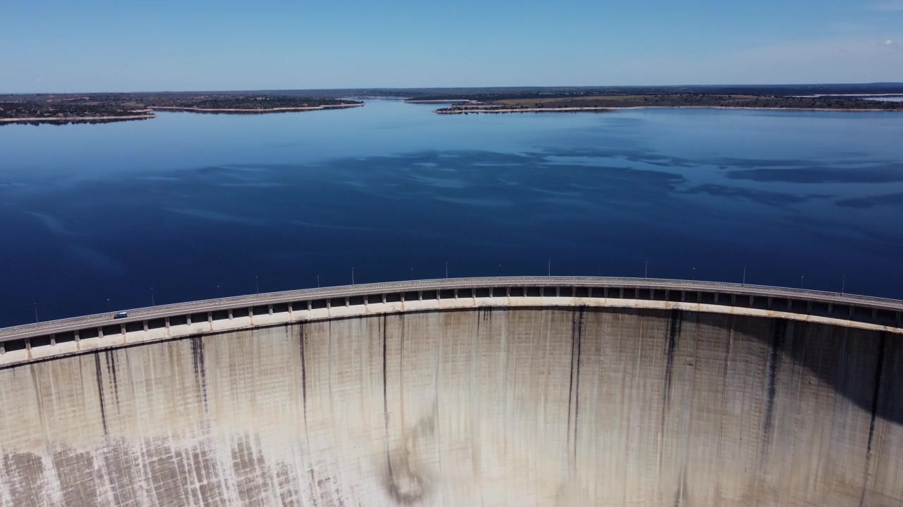 4K luftdronevideo med et bredt totalbillede af den massive frontside af Almendra-dæmningen i Salamanca, Spanien. De imponerende optagelser fanger den enorme buede betonmur, højtryksvand