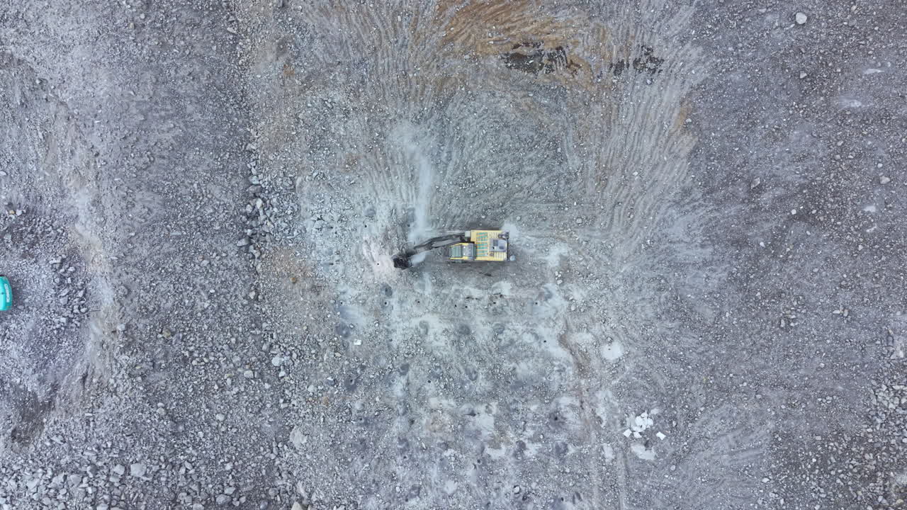 Excavator operates on gravel site in countryside during daylight hours of early spring 2023