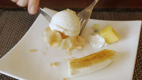 Usando-Un-Tenedor-Para-Comer-Gofres-Croffle-En-Un-Plato-Con-Helado-Y-Banana-Caramelizada