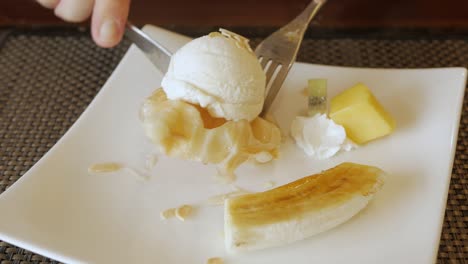 usando un tenedor para comer gofres croffle en un plato con helado y banana caramelizada