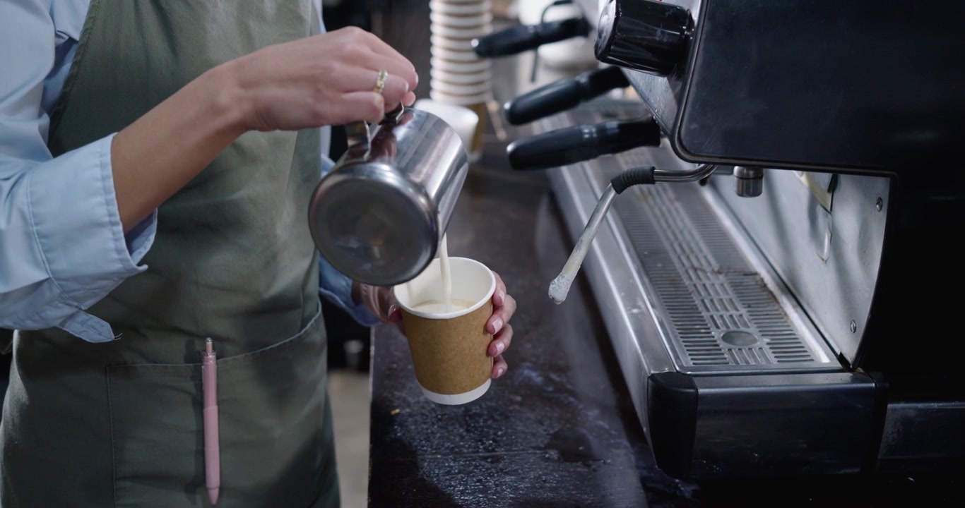 Un barista gira la manopola del vapore, monta il latte in una brocca di metallo, versandolo in un bicchiere di carta per servire.