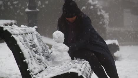 Woman-building-a-snowman-on-a-bench-during-winter-in-Tbilisi,-Georgia