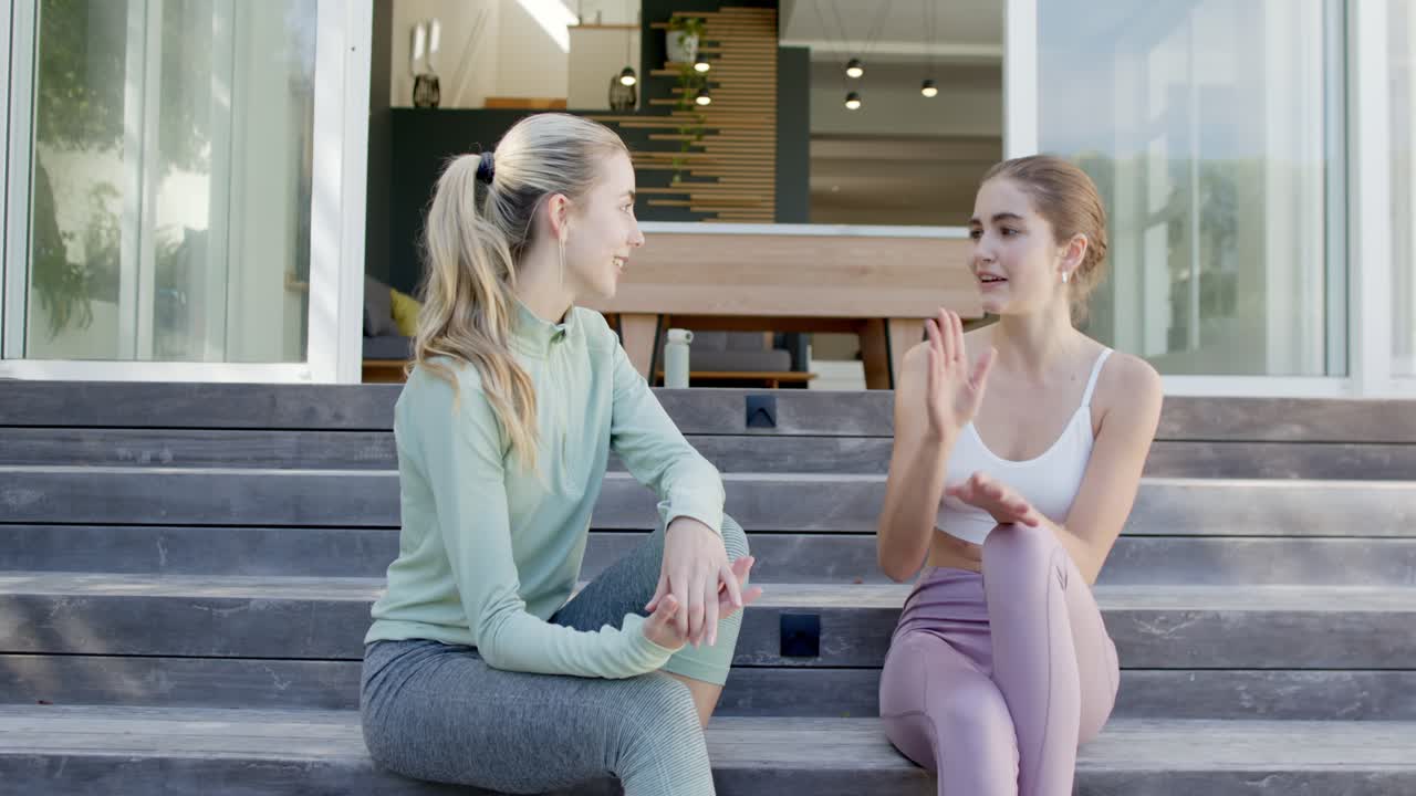 Female friends starting conversation on wooden patio steps using gestures high fiving and laughing