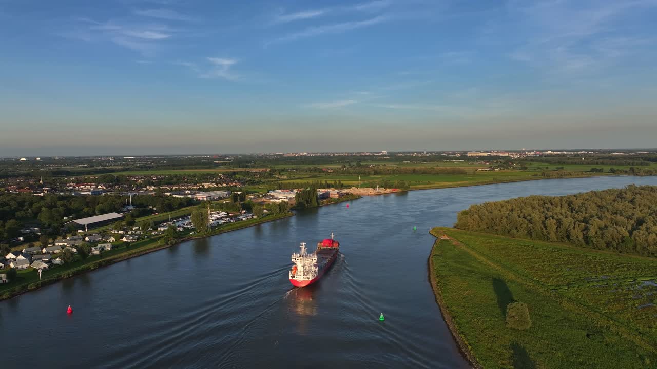 Aerial view of cargo ship cruising down a river surrounded by green landscapes