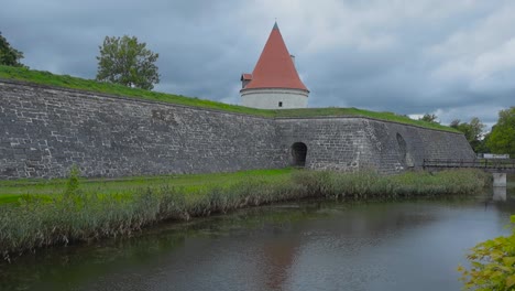 un foso lleno de agua ondulada y reflectante fuera del castillo de kuressaare con un puente de madera que atraviesa el agua