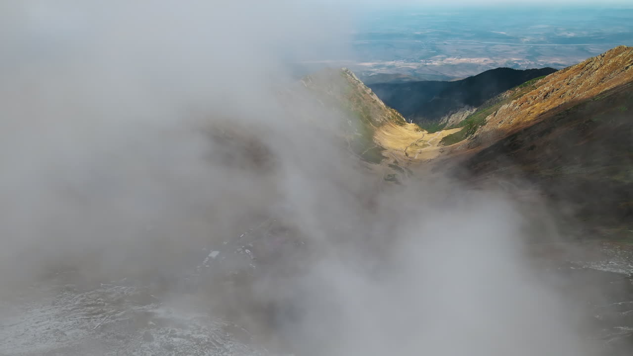 Aerial drone view of nature in Romania. Transfagarasan route in Carpathian mountains, Balea Lake resort and rocky slopes, valley, clouds