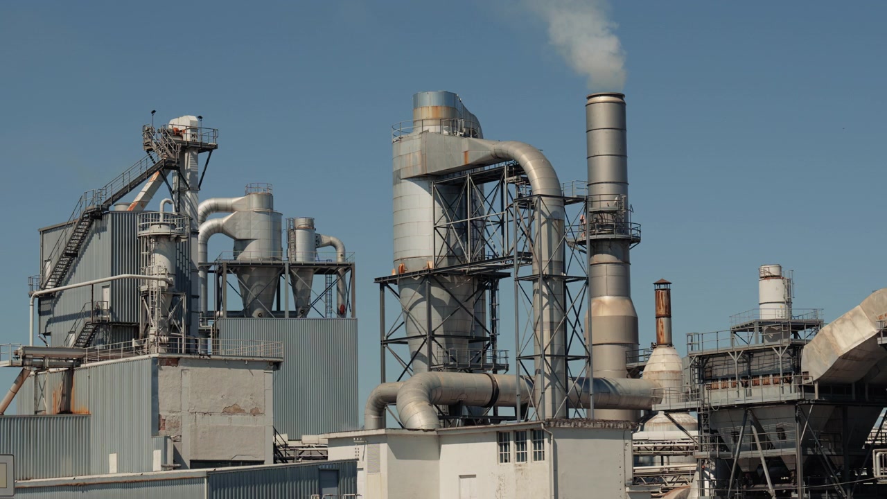 Industrial factory complex Lesonit with large metal processing structures and smoking chimney under clear blue sky. Manufacturing and wood chemical industry facility in Slovenia.