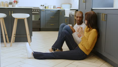multiracial couple relaxing on kitchen floor, enjoying coffee and conversation together, at home