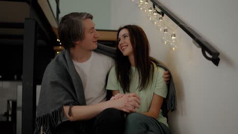 Young-couple-relaxing-on-wooden-stairs,-embracing-each-other