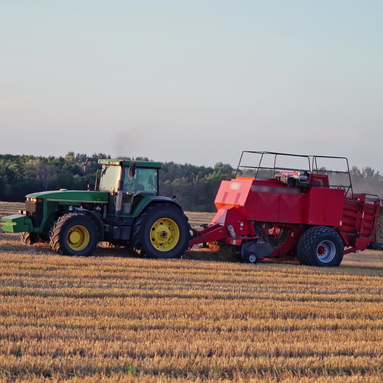 Harvesting dry grass. Agricultural works in the field. Tractor is pressing hay into square bale on the natural yellow field background.