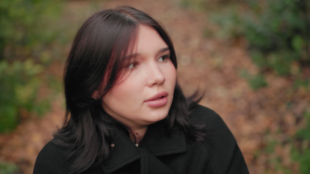 숲 속을 거닐면서 담요로 몸을 가리고 있는 어린 소녀의 시선이 위로 향한 모습, 쌀쌀한 가을 길에서 코트 깃을 스웨터 위로 잡아당기는 손, 발밑의 부드러운 낙엽, 조용한 자연 속 산책