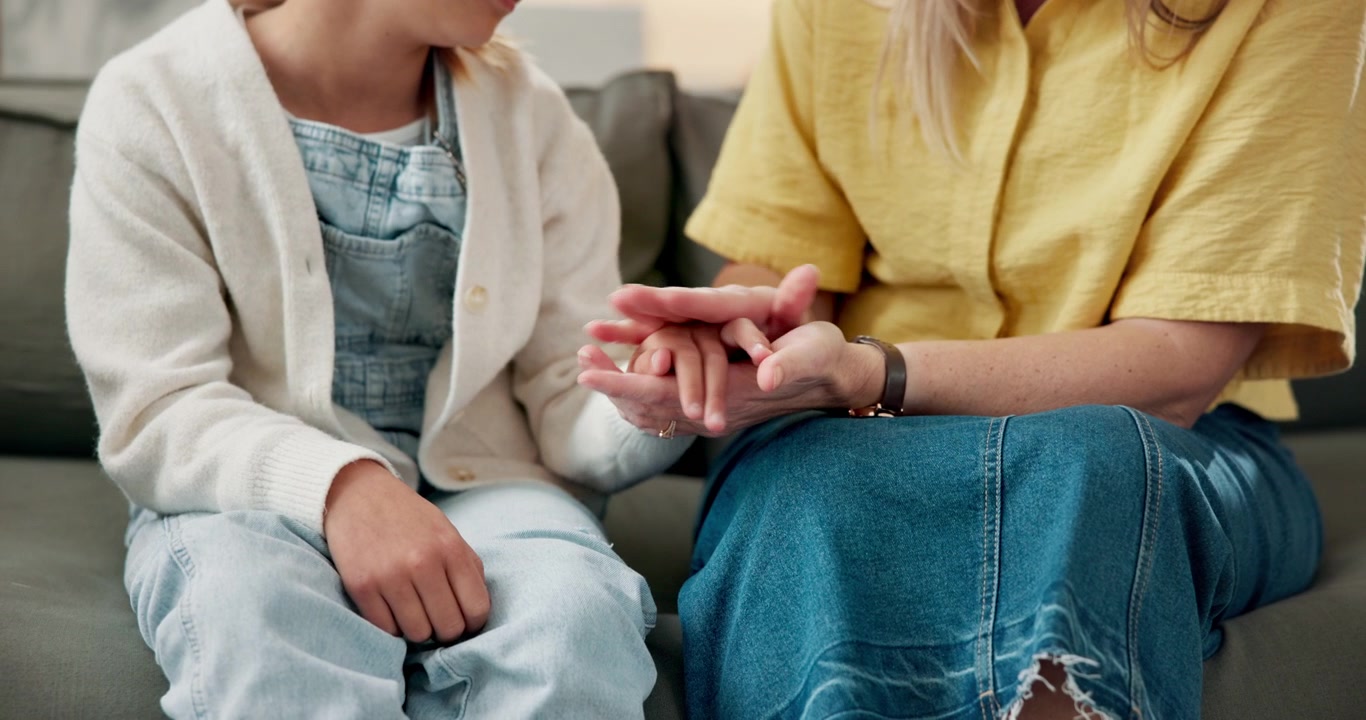 Madre che conforta la figlia tenendole le mani sul divano