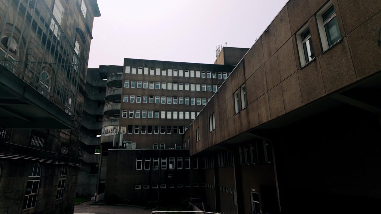 L'architettura brutalista si erge imponente contro un cielo coperto, mostrando un moderno edificio in cemento con numerose finestre e un'intrigante scala esterna curva. Architettura tradizionale più antica